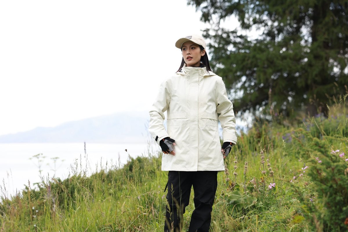 Hiker in a white hardshell jacket above a mountain lake - Understanding Outdoor Jacket Fabric Technologies: Complete B2B Guid