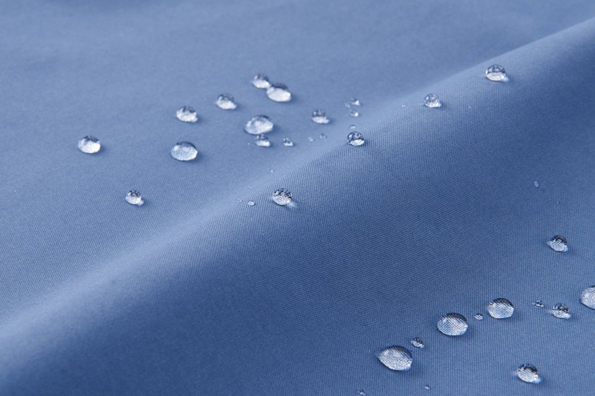 Water beading on the DWR face of a light blue shell fabric - YKK Waterproof Zipper Jacket Sourcing Guide (2026)